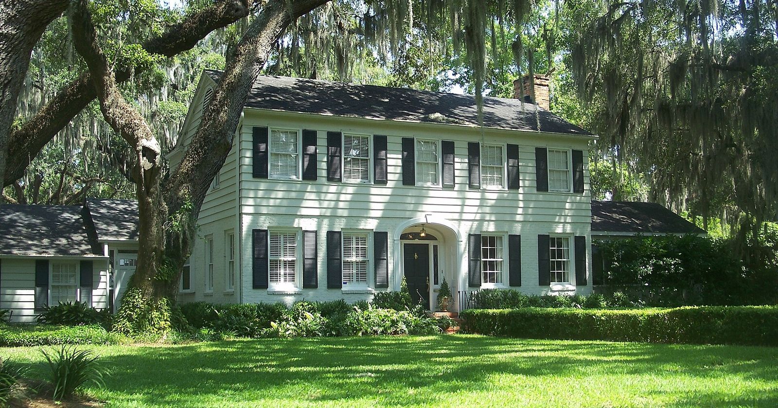 A white colonial house with black shutters under live oaks and Spanish moss in Old Ortega, Jacksonville