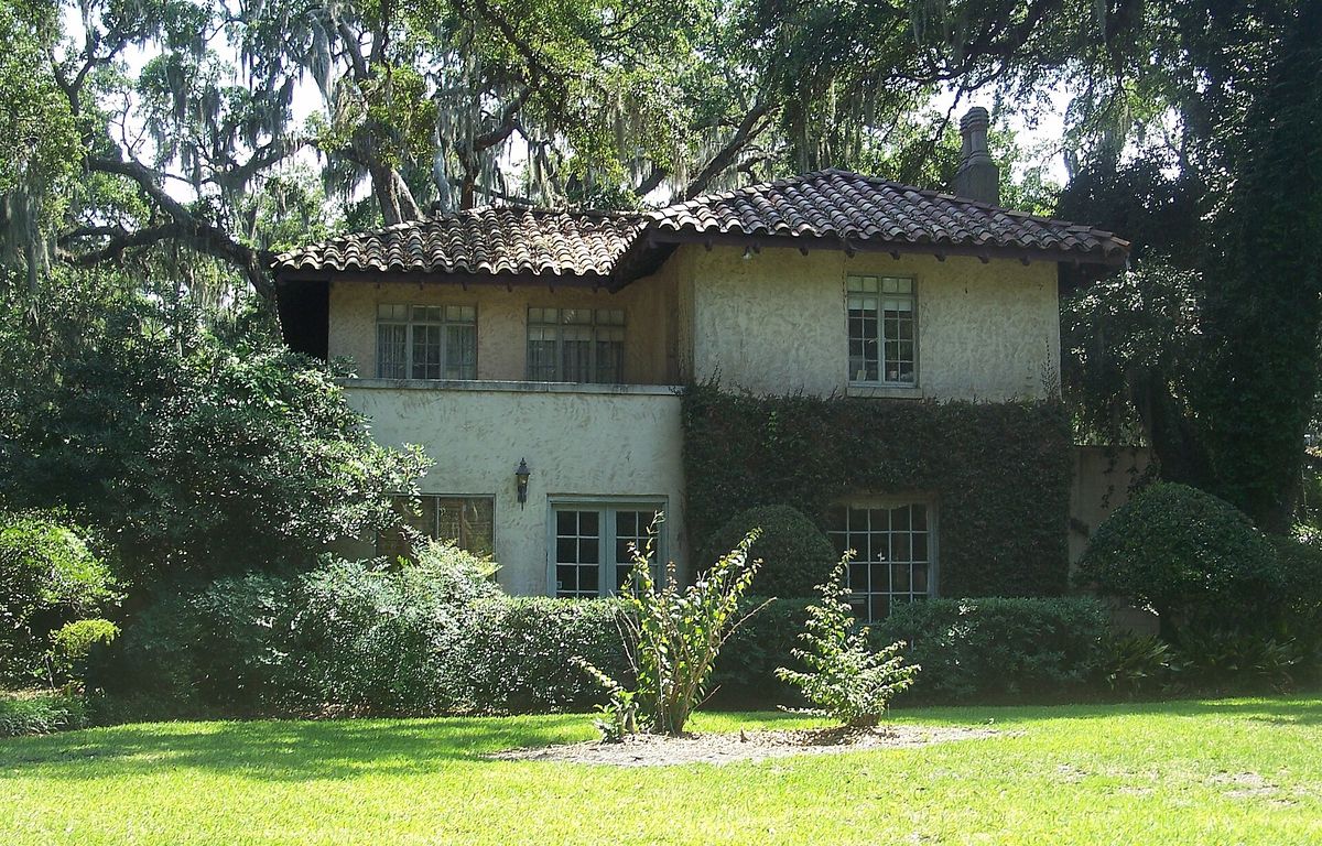 A two-story stucco house with a clay tile roof under live oaks in Old Ortega, Jacksonville
