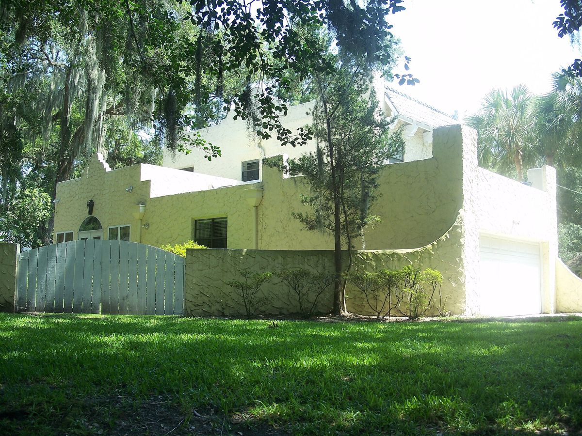 A yellow stucco house with a curved wall and garage under live oaks in Old Ortega, Jacksonville
